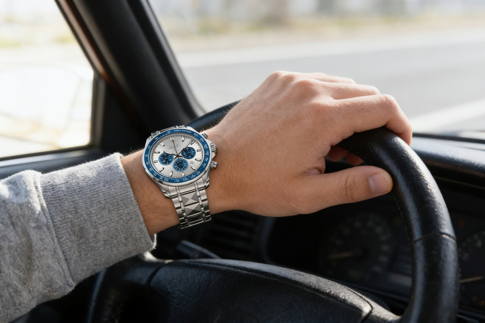 A steel chronograph on a wrist resting on a car steering wheel