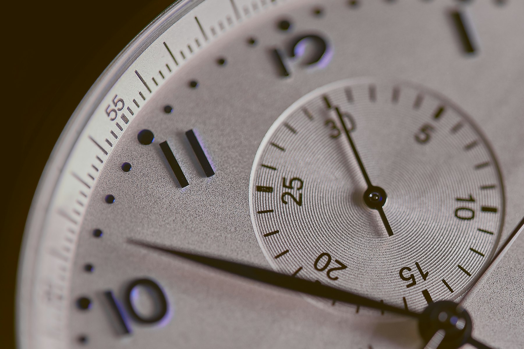 Close up of a silver dial with raised Arabic numerals and a small seconds subdial