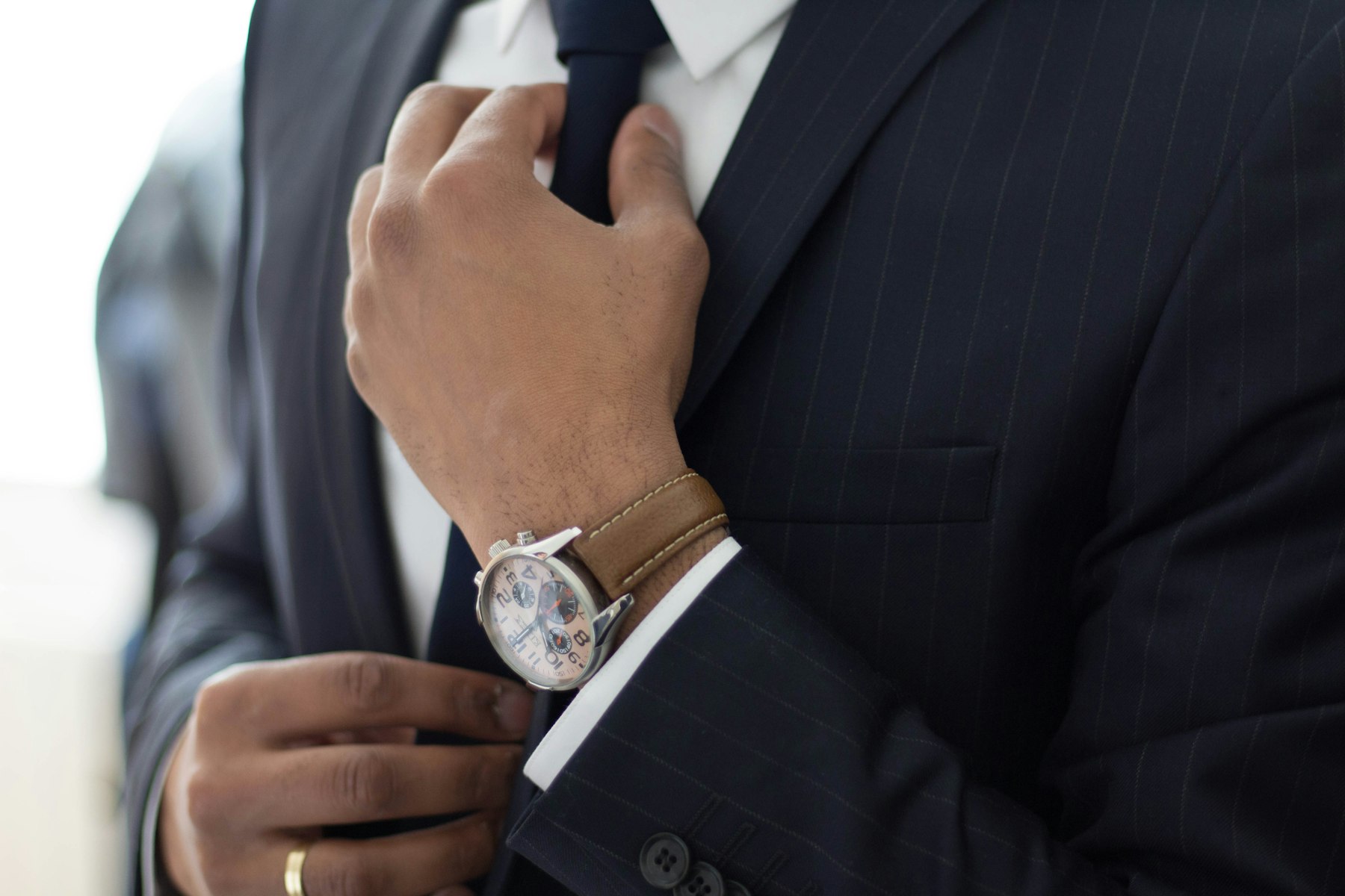 Man in a pinstripe suit straightening his tie while wearing a pilot style chronograph