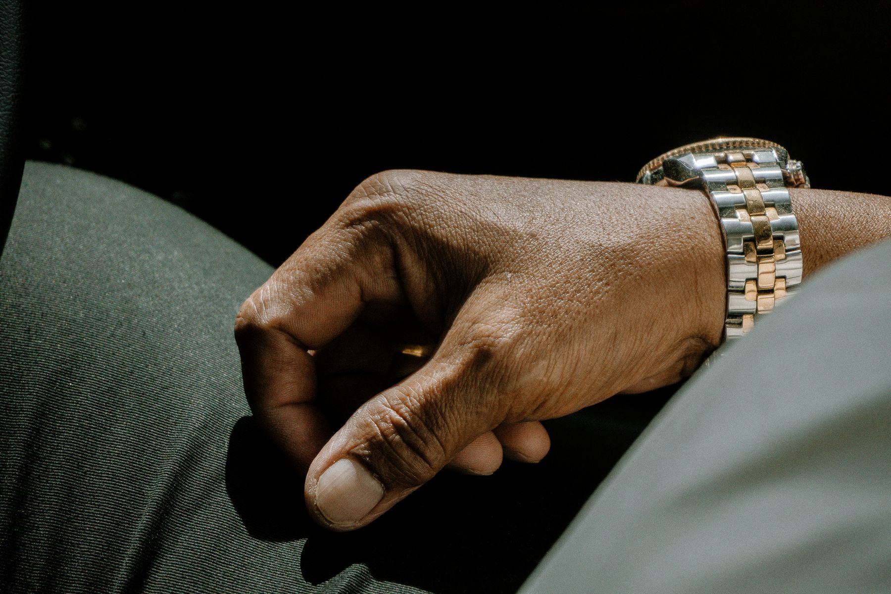 A hand resting on a knee with a silver and gold two tone bracelet watch