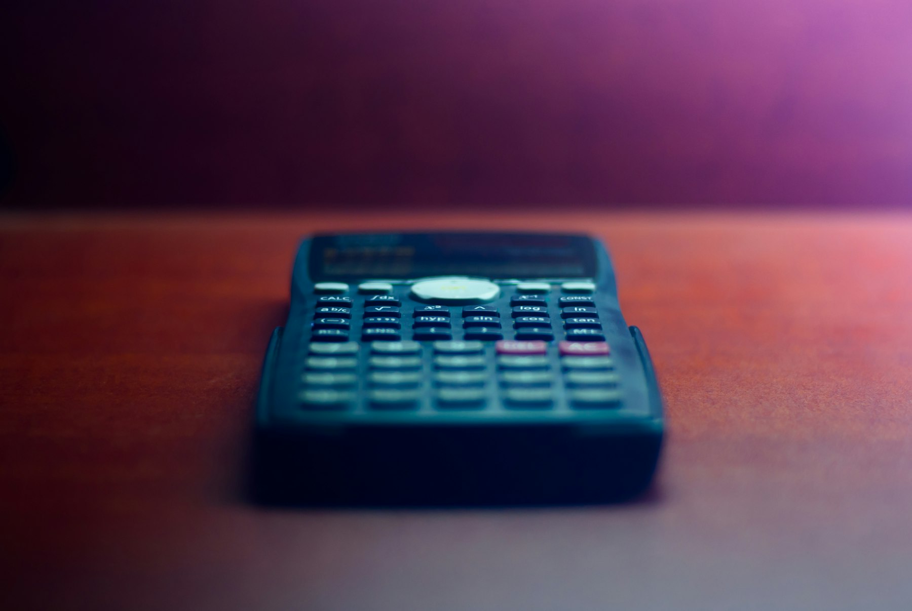 A dark calculator on a wooden desk under soft purple light