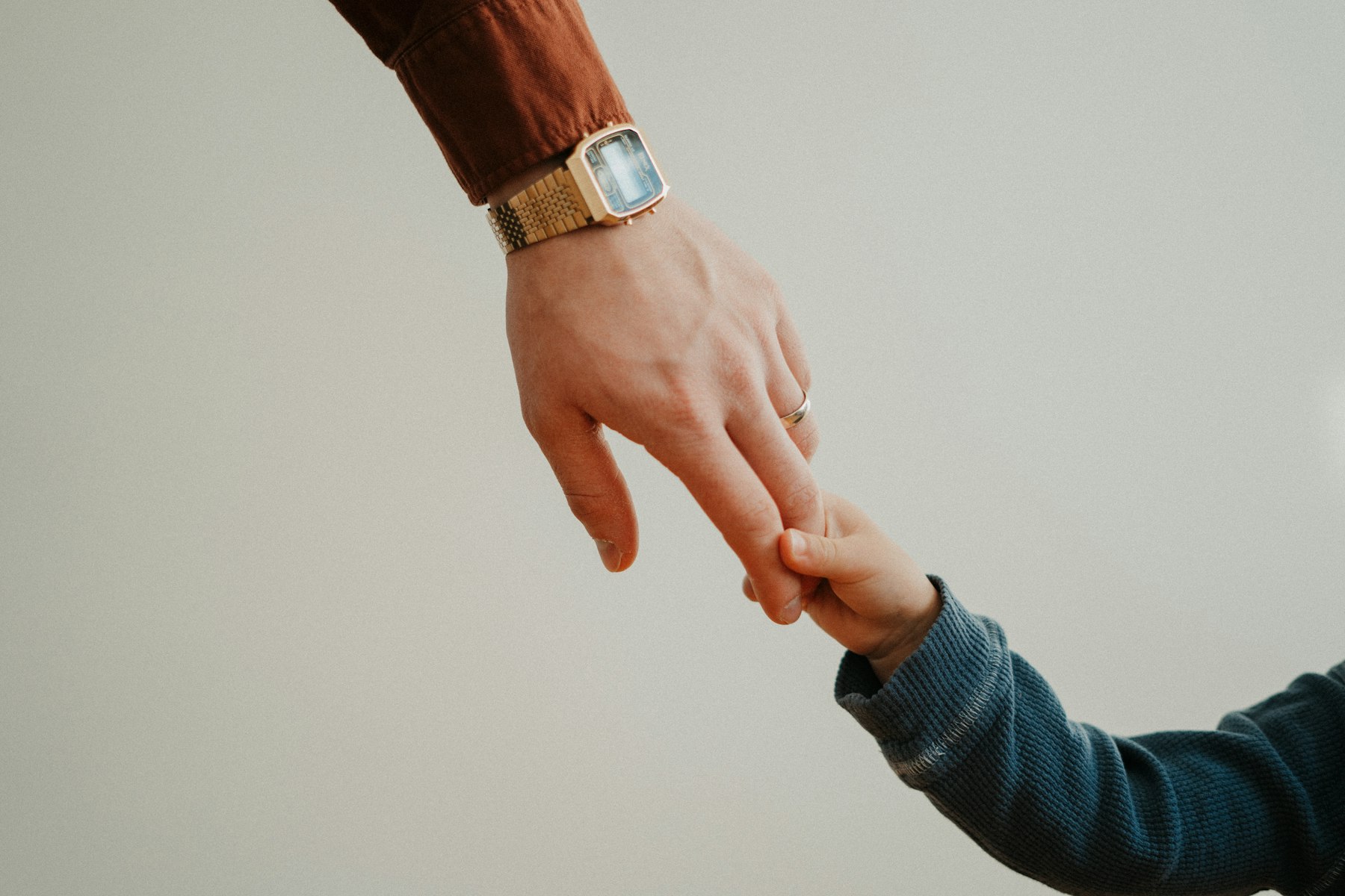 A man wearing a gold tone square watch holds a small child's hand