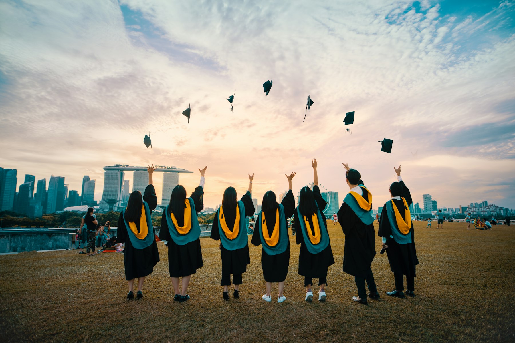 Graduates in gowns throwing their caps into the air against a city skyline