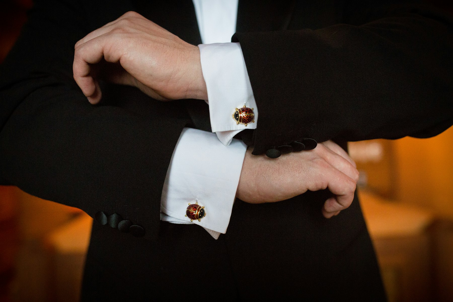 Hands adjusting red cufflinks on a white shirt under a dark suit