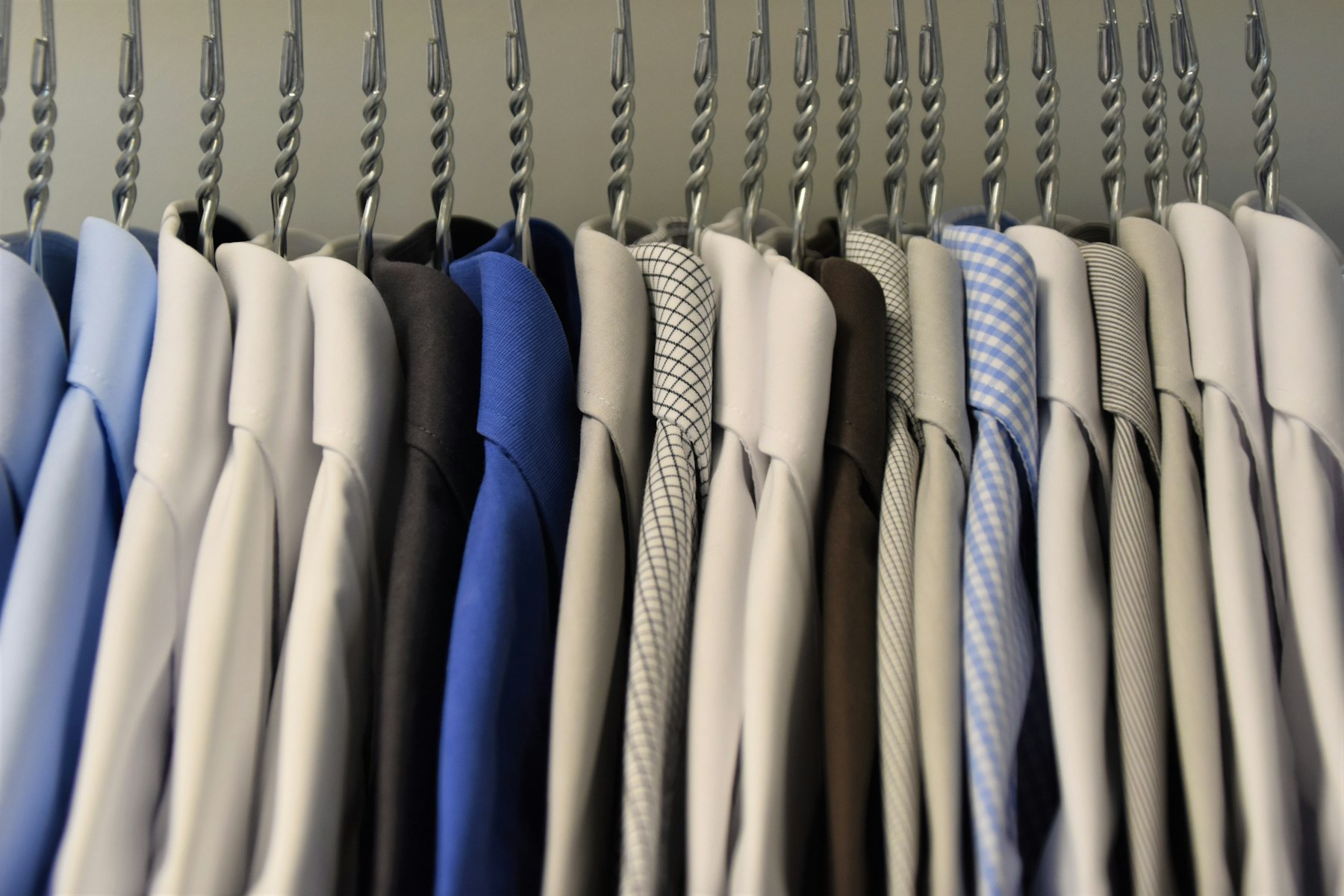 A row of dress shirts in white, blue, grey and check hanging in a wardrobe