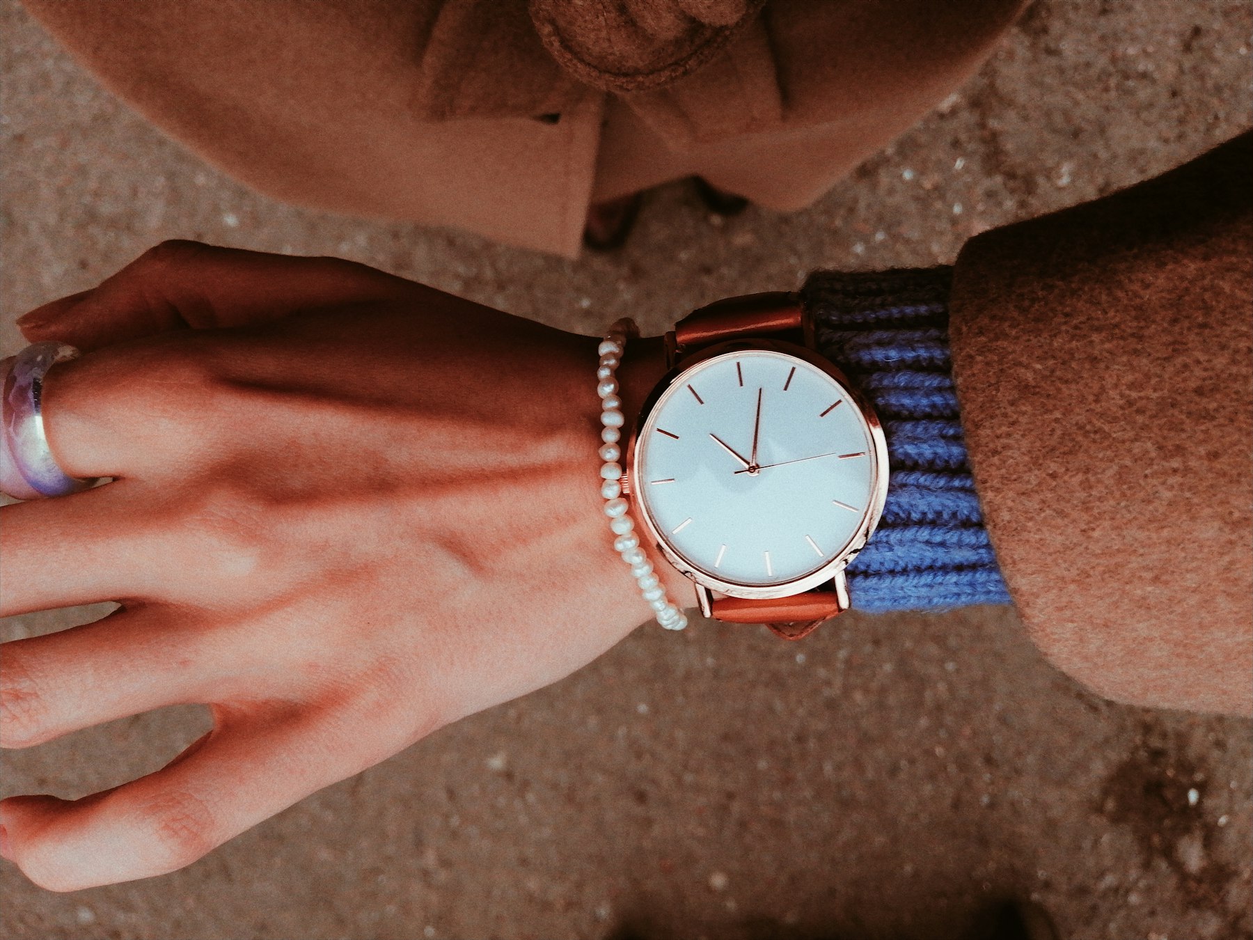 A rose gold watch on a leather strap worn next to a small pearl bracelet