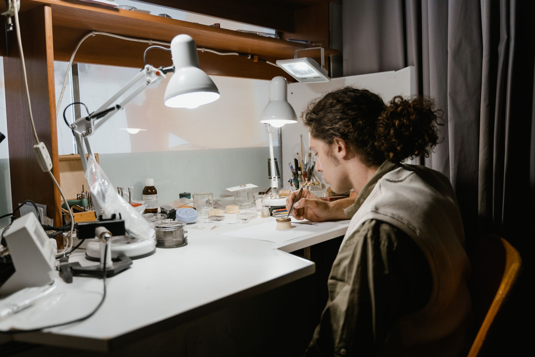 A young watchmaker working at a bench under desk lamps with tools and parts