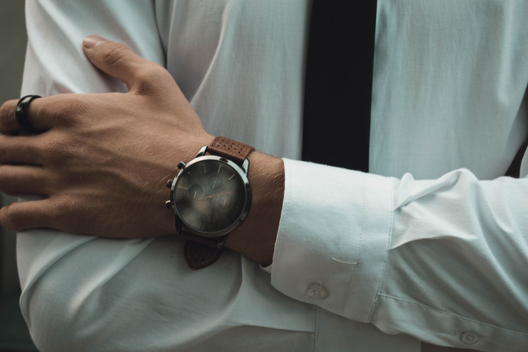 Folded arms in a white shirt showing a dark chronograph on a perforated leather strap