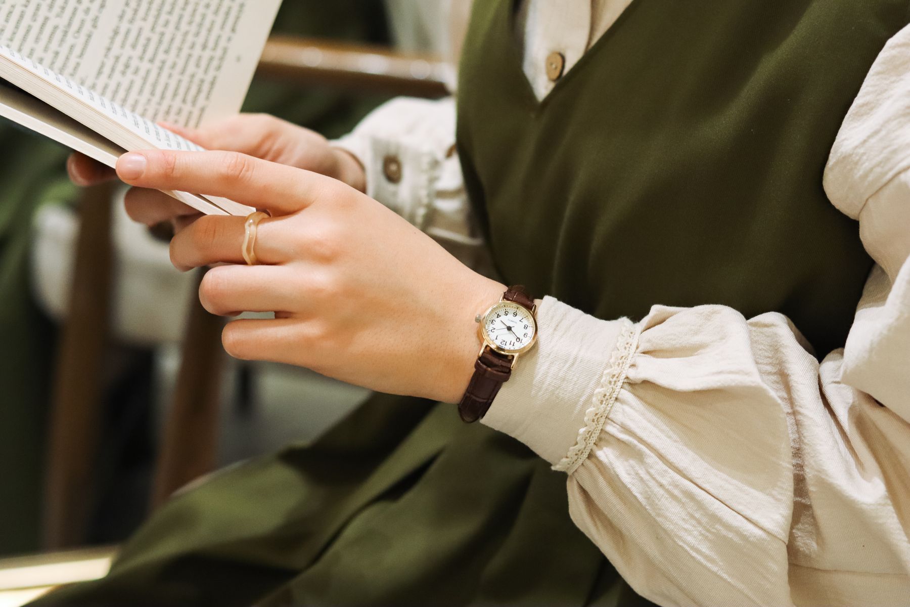 A woman reading a book wearing a tiny gold watch with a white dial on a brown strap